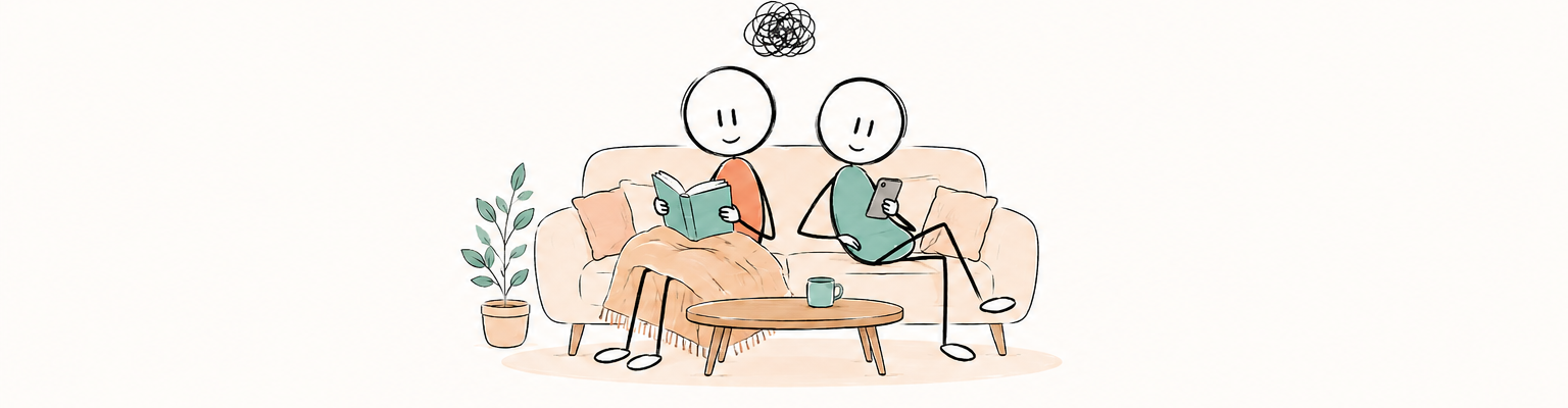 Deux partenaires confortablement installé.e.s dans un salon, l’un.e lit sous un plaid tandis que l’autre regarde son téléphone, avec une petite pelote emmêlée au-dessus d’eux.